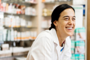 Female pharmacist smiling with teeth and leaning over a counter