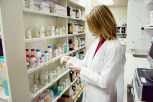 Female pharmacist examining medication in front of a row of shelves