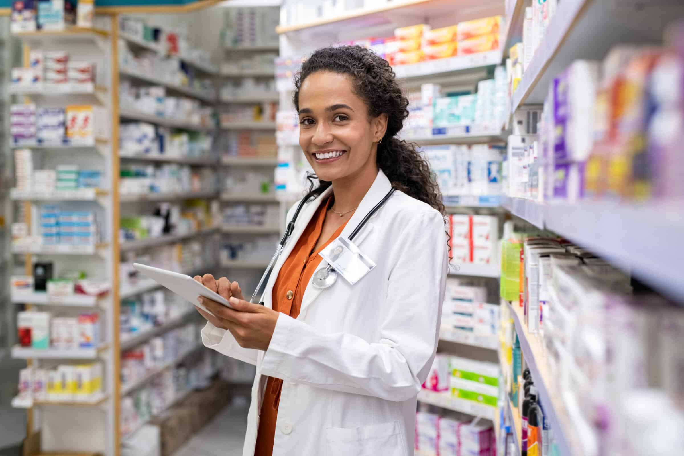 A pharmacist looking toward a camera and smiling in a pharmacy.