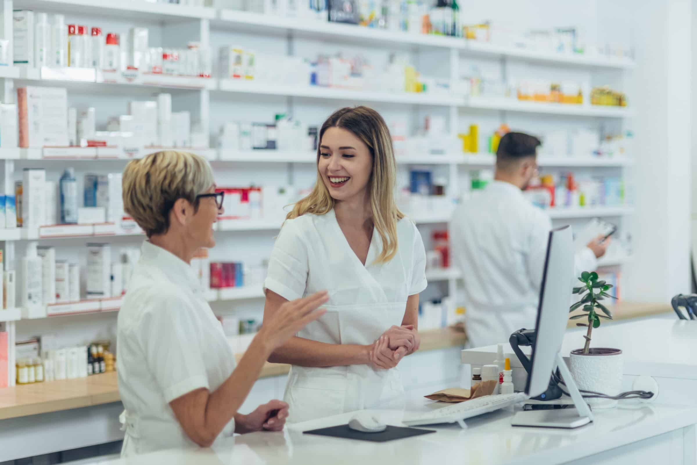 Two pharmacists smiling at each other at a pharmacy counter.