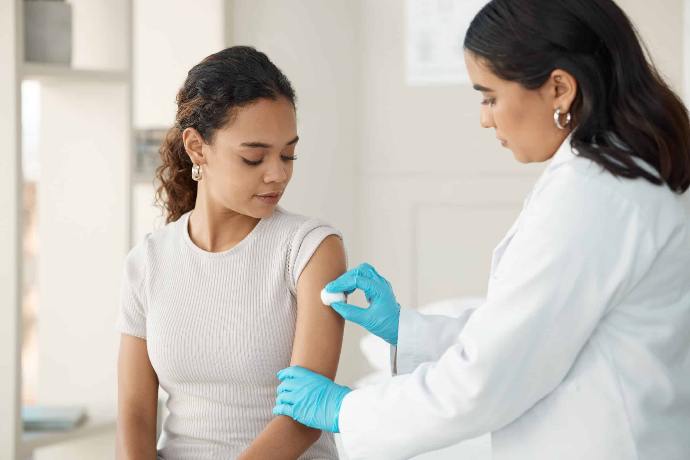 A pharmacist is cleaning the upper arm of a client, preparing to give them an injection.