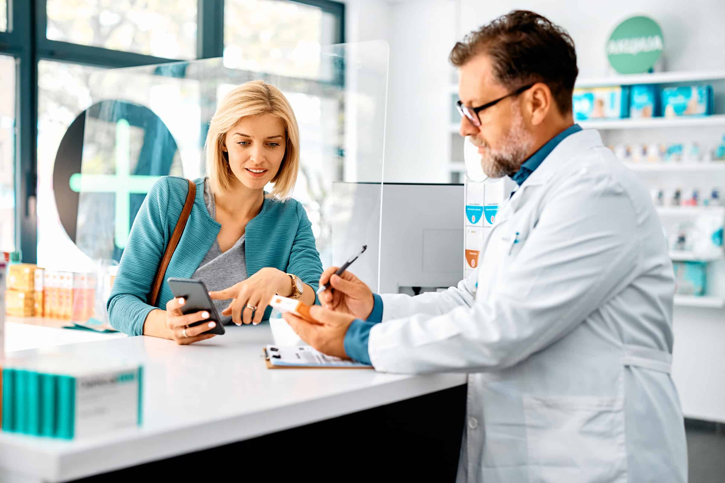 A pharmacist talking to a client about their prescription while the client points to their phone.