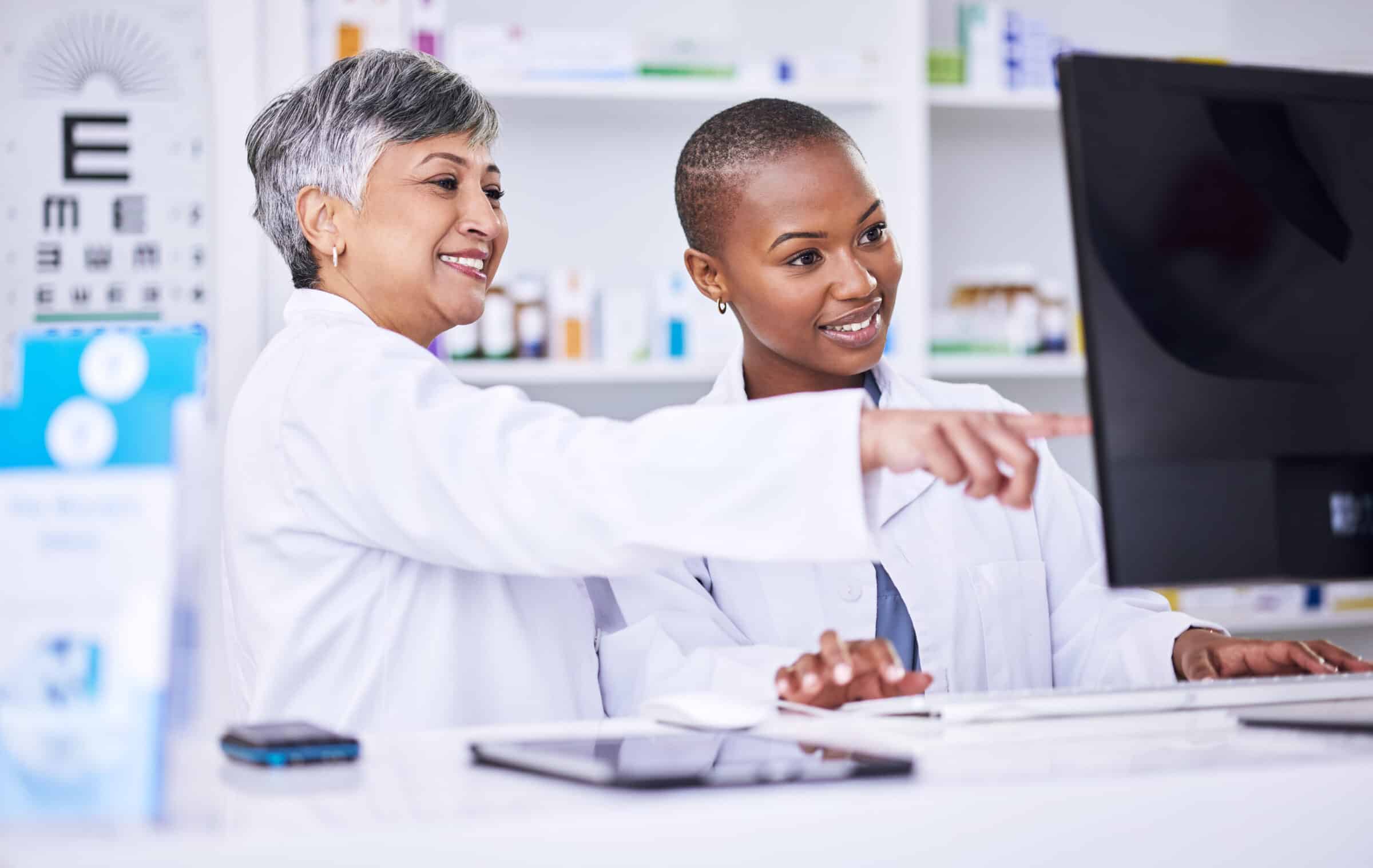 Two pharmacists looking at a computer screen. One is pointing to the computer screen.