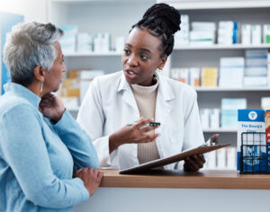 A pharmacist engaging in conversation with a female patient and taking notes on a clipboard.