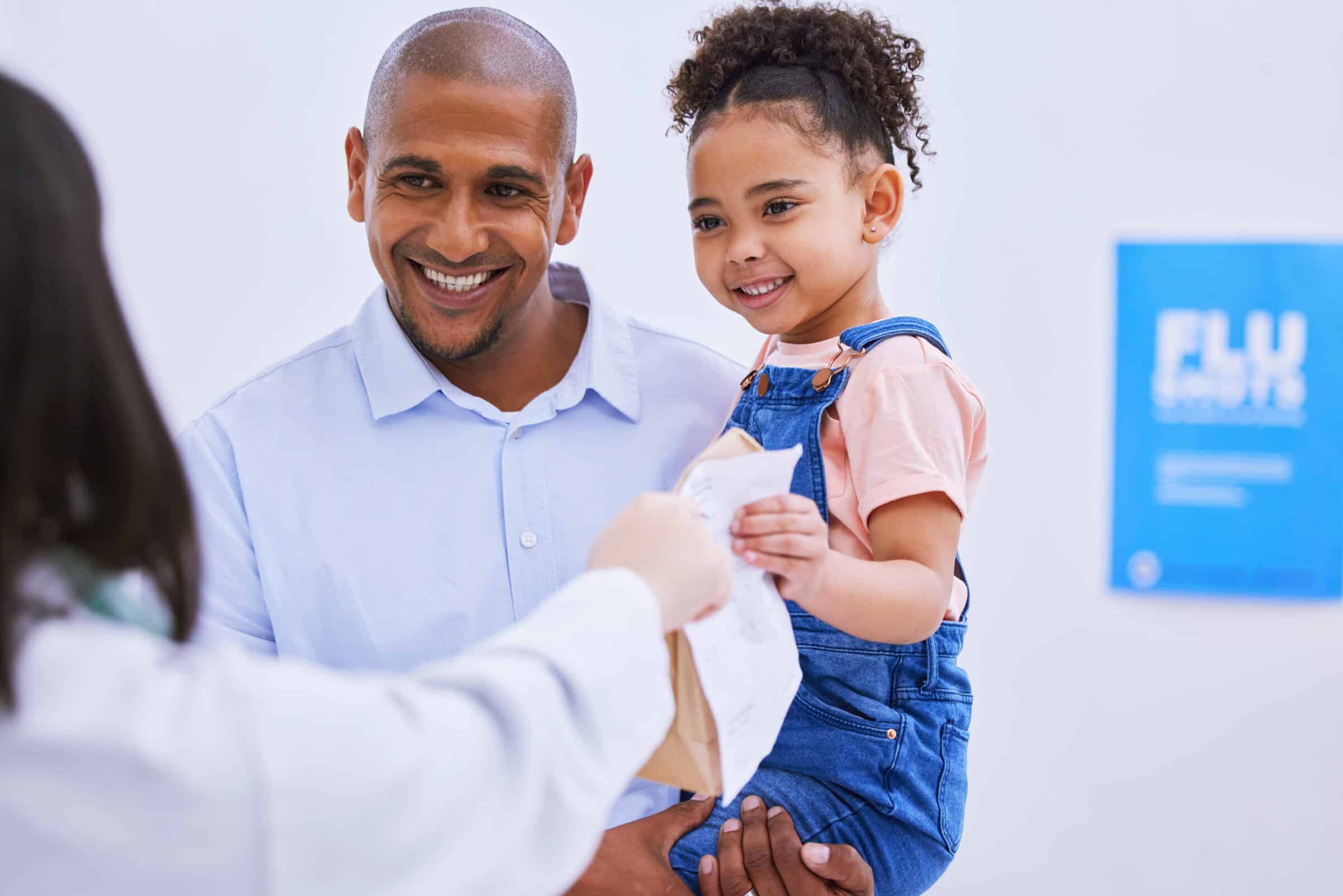 A pharmacist is handing a prescription bag to a client holding a child.